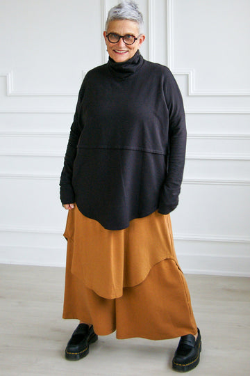 Woman wearing black oversized turtleneck tencel Abigail top by Advika, over ochre dress and wide leg pants. 