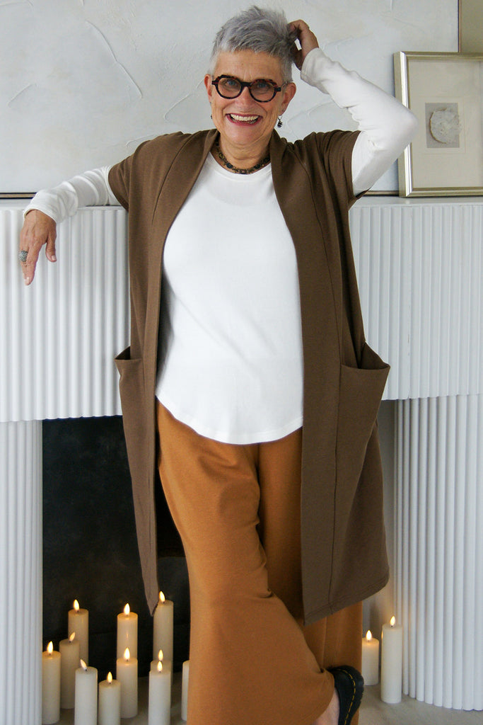 Woman wearing long sleeve white tencel top, brown open front short sleeve cardigan and wide leg pants. 